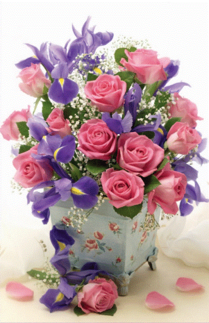 Roze rozen en paarse irissen in een decoratieve, blauwe vaas met bloemmotief. Enkele rozenblaadjes op de voorgrond.