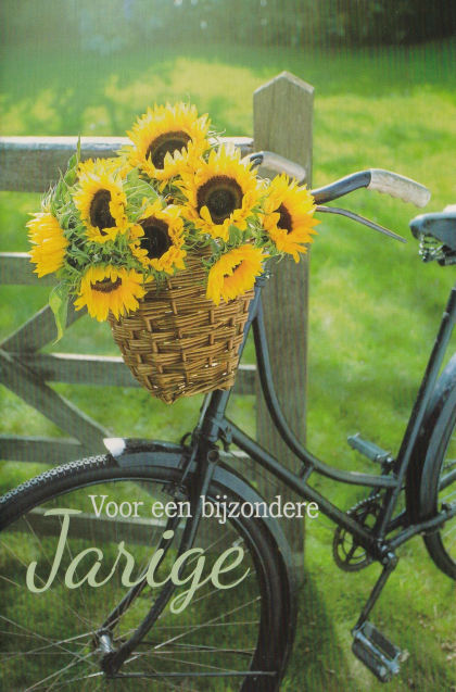 Fiets met mand vol zonnebloemen tegen hek, groene achtergrond. Tekst: "Voor een bijzondere Jarige".